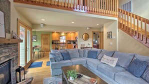 A spacious living room with a large grey sectional sofa, a wooden coffee table, and a fireplace. A wooden staircase leads to an upper level. - Wintergreen Resort Cabin: Near the Slopes! (Wintergreen Resort)