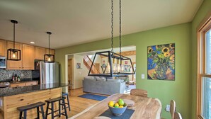 A modern kitchen with wooden cabinets, a stainless steel refrigerator, and a dining area with a wooden table and stools. - Wintergreen Resort Cabin: Near the Slopes! (Wintergreen Resort)
