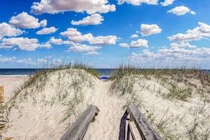 A sandy beach path leading to the ocean with a wooden boardwalk and beach grass.