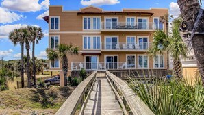 A multi-story building with balconies, a wooden walkway, and palm trees. - Sea Breeze | Large 1 BR, 2 BA Oceanview Condo! (Fernandina Beach)