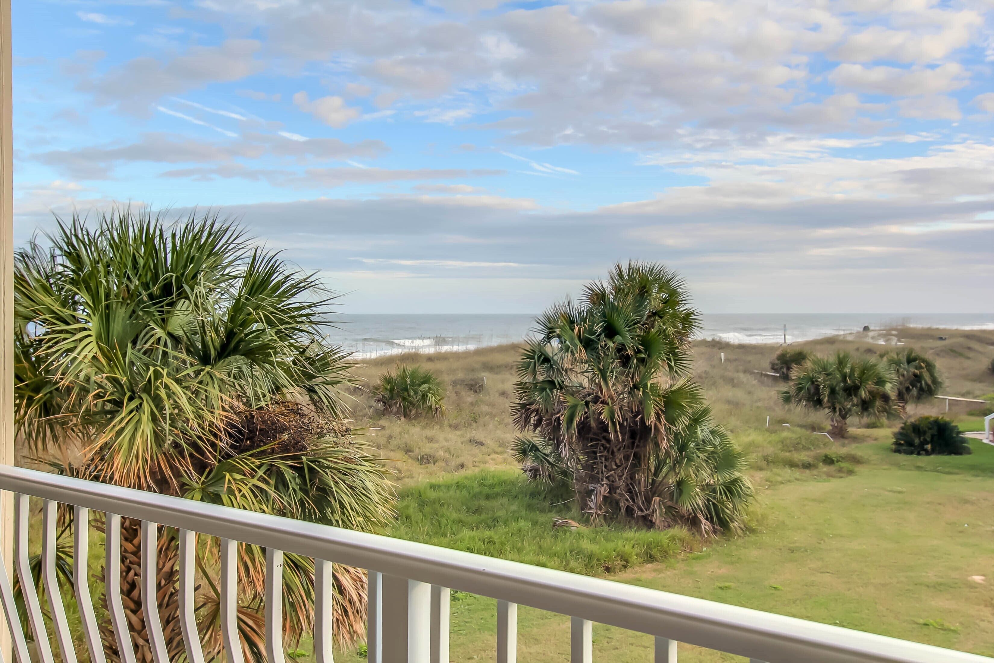 A balcony with a view of the ocean and grassy landscape.