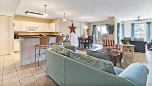 A spacious living area with a sofa, dining table, and chairs. A kitchen with white cabinets and a microwave is visible. - Sea Breeze | Large 1 BR, 2 BA Oceanview Condo! (Fernandina Beach)