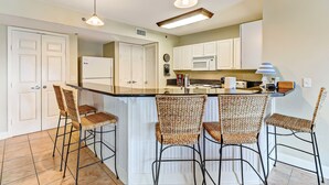 A kitchen with a central island, white cabinets, and bar stools. - Sea Breeze | Large 1 BR, 2 BA Oceanview Condo! (Fernandina Beach)