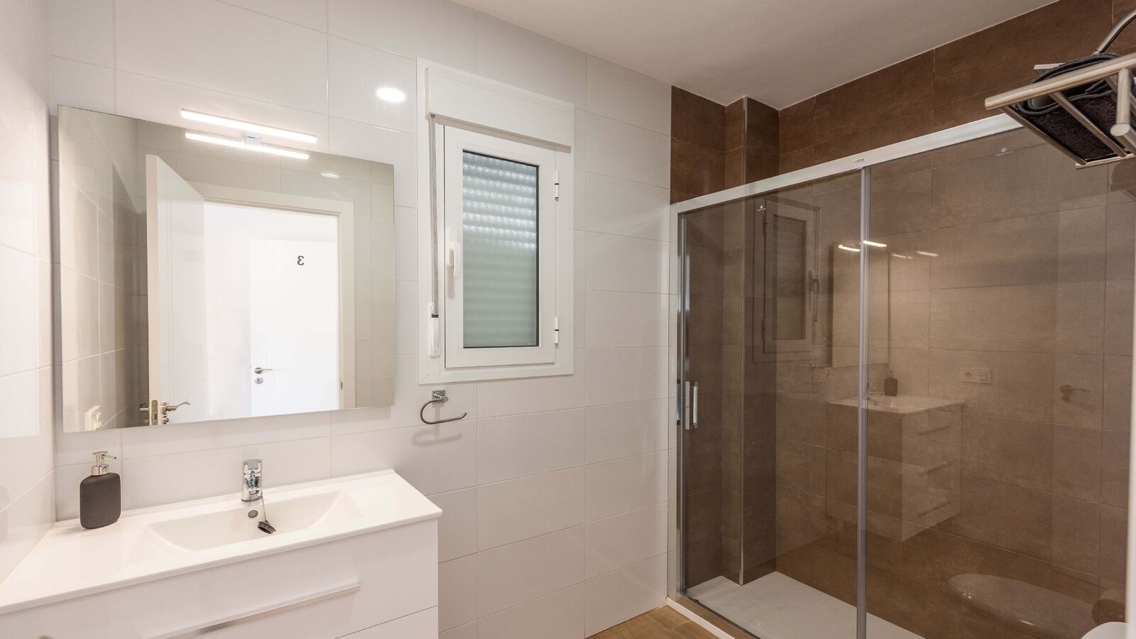 A modern bathroom with a glass shower enclosure, a white vanity, and a large mirror.