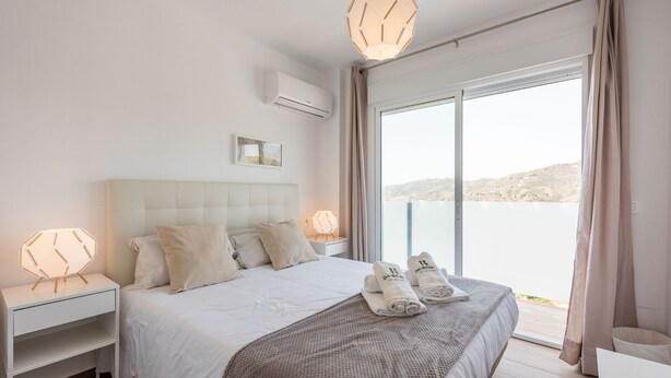 A modern hotel bedroom with a large bed, two bedside tables, a nightstand, a view of the sea, and a balcony with a railing. - Villa Esperanza Canillas de Albaida by Ruralidays (Málaga)