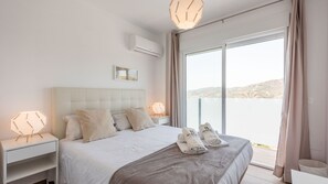 Ein modernes Hotelzimmer mit einem großen Bett, zwei Nachttischen, einem Beistelltisch, Meerblick und einem Balkon mit Geländer.