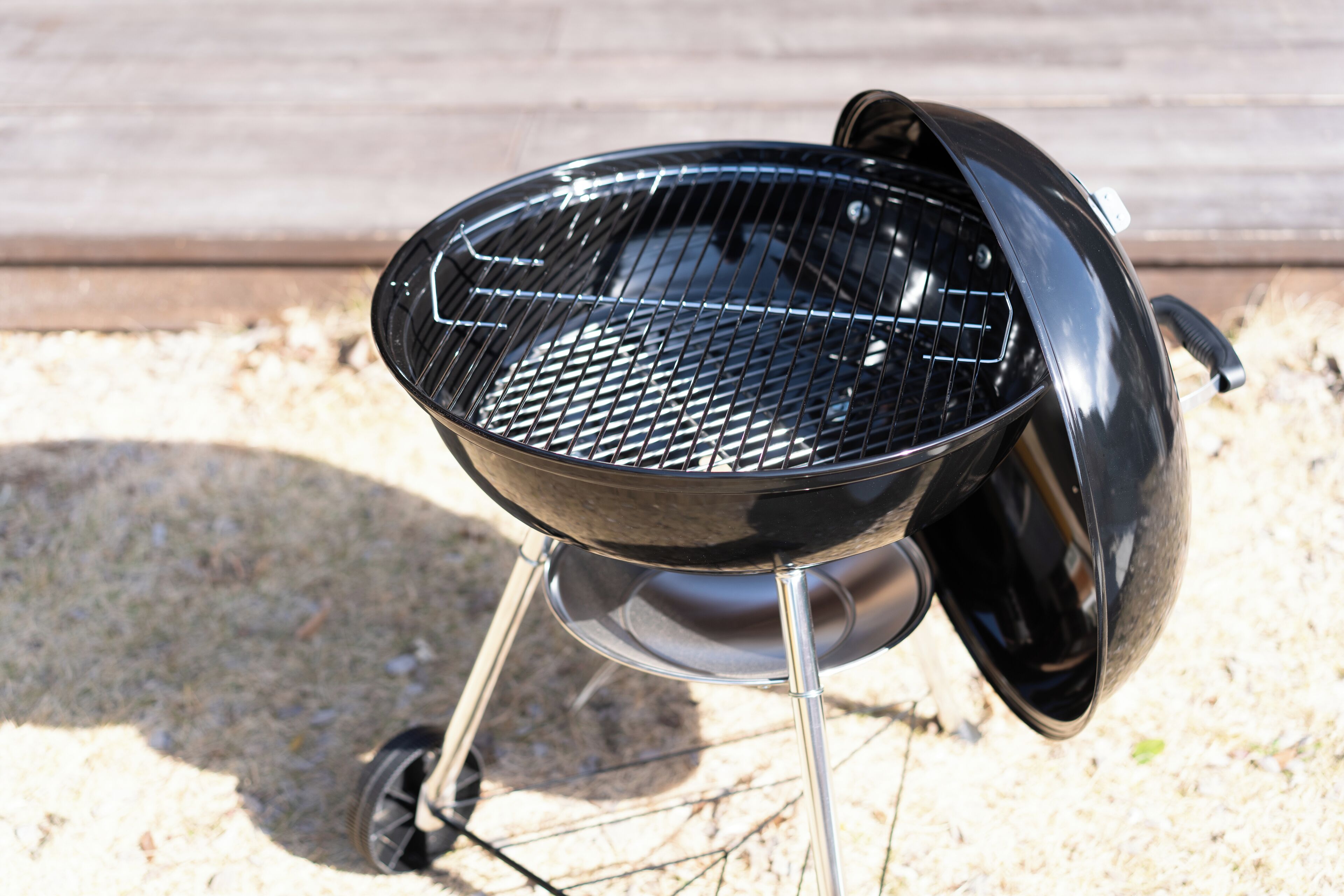 En svart grill med ett galler, placerad utomhus på ett underlag av grus.