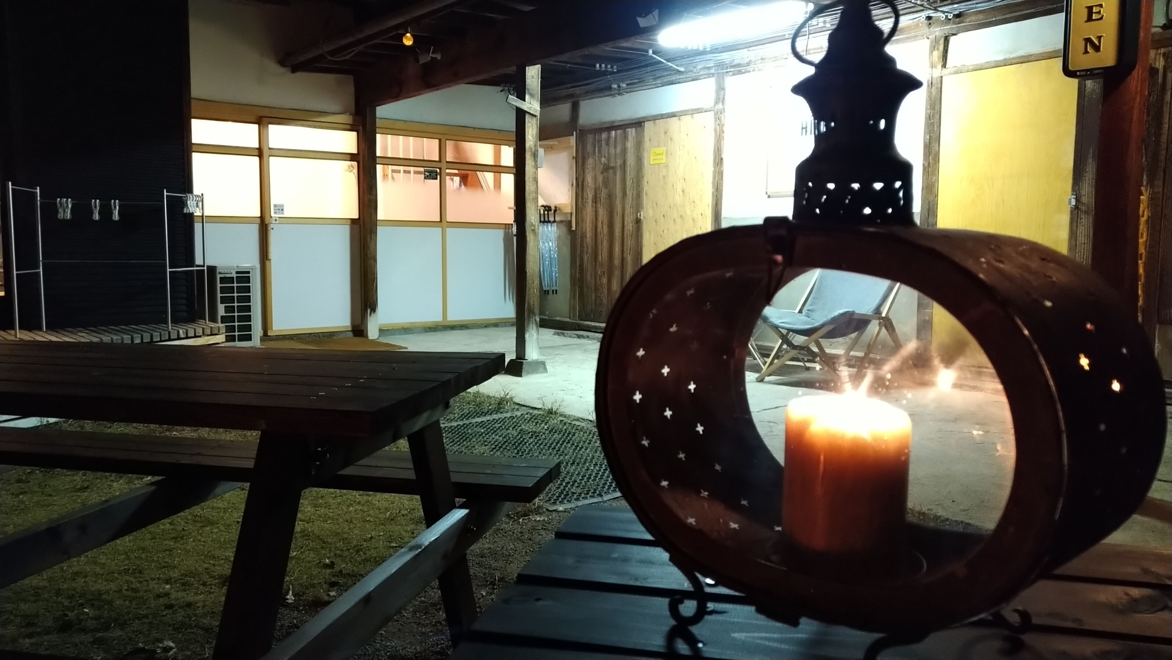 A wooden table and bench in a covered outdoor area with a lit candle in a decorative holder.