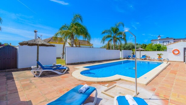 A swimming pool with lounge chairs and a thatched umbrella. - Casas Villanueva - Casa Familiar Conil de la Frontera by Ruralidays (Cádiz)