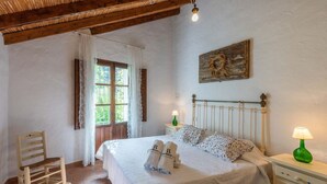 A bedroom with a wooden bed, a nightstand, a chair, and a window with curtains. - Molino Maroto Alhaurín el Grande by Ruralidays (Málaga)