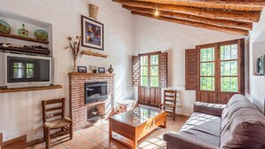 A cozy living room with a fireplace, wooden furniture, and large windows. - Molino Maroto Alhaurín el Grande by Ruralidays (Málaga)