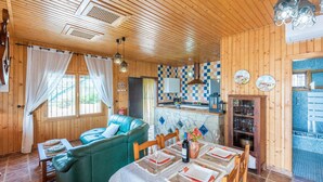 Un intérieur de chalet chaleureux avec un coin repas, un canapé et une cuisine dont le mur derrière l’évier est recouvert de carreaux.