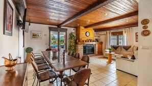 A spacious dining area with a long wooden table and chairs, a fireplace, and a cozy seating area with a sofa and a small side table.