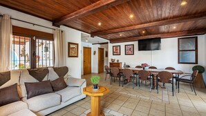 A living room with a sofa, dining table, chairs, and a TV mounted on the wall.