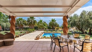 An outdoor pool area with a covered patio, stone seating, and a table with chairs.