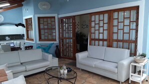 Una sala de estar con sofás blancos, una mesa de centro de vidrio y piso de piedra.