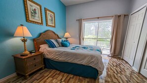 A bedroom with a wooden herringbone floor, a bed with blue bedding, two bedside lamps, and two framed pictures on the wall. - Lovely 3BR 2 Bath Orlando Area Resort Condo (Davenport)