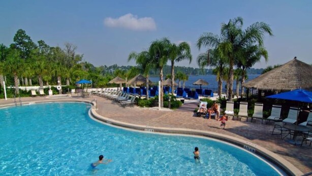 A swimming pool with lounge chairs and umbrellas, surrounded by palm trees and a clear sky. - Lovely 3BR 2 Bath Orlando Area Resort Condo (Davenport)