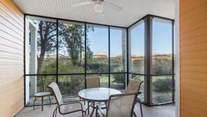 Eine verglaste Terrasse mit rundem Tisch und vier Stühlen, die einen Blick auf einen angelegten Garten und ferne Hügel bietet.