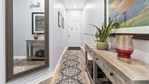 Un couloir avec un tapis à motifs, un miroir, une console sur laquelle est posé un vase, et une porte au fond.