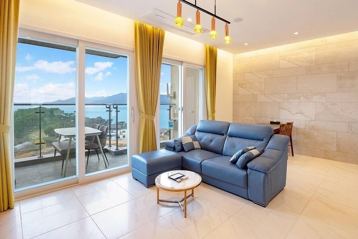 A modern living room with a blue sectional sofa, a small round coffee table, and a large sliding glass door leading to an outdoor balcony with a table and chairs.