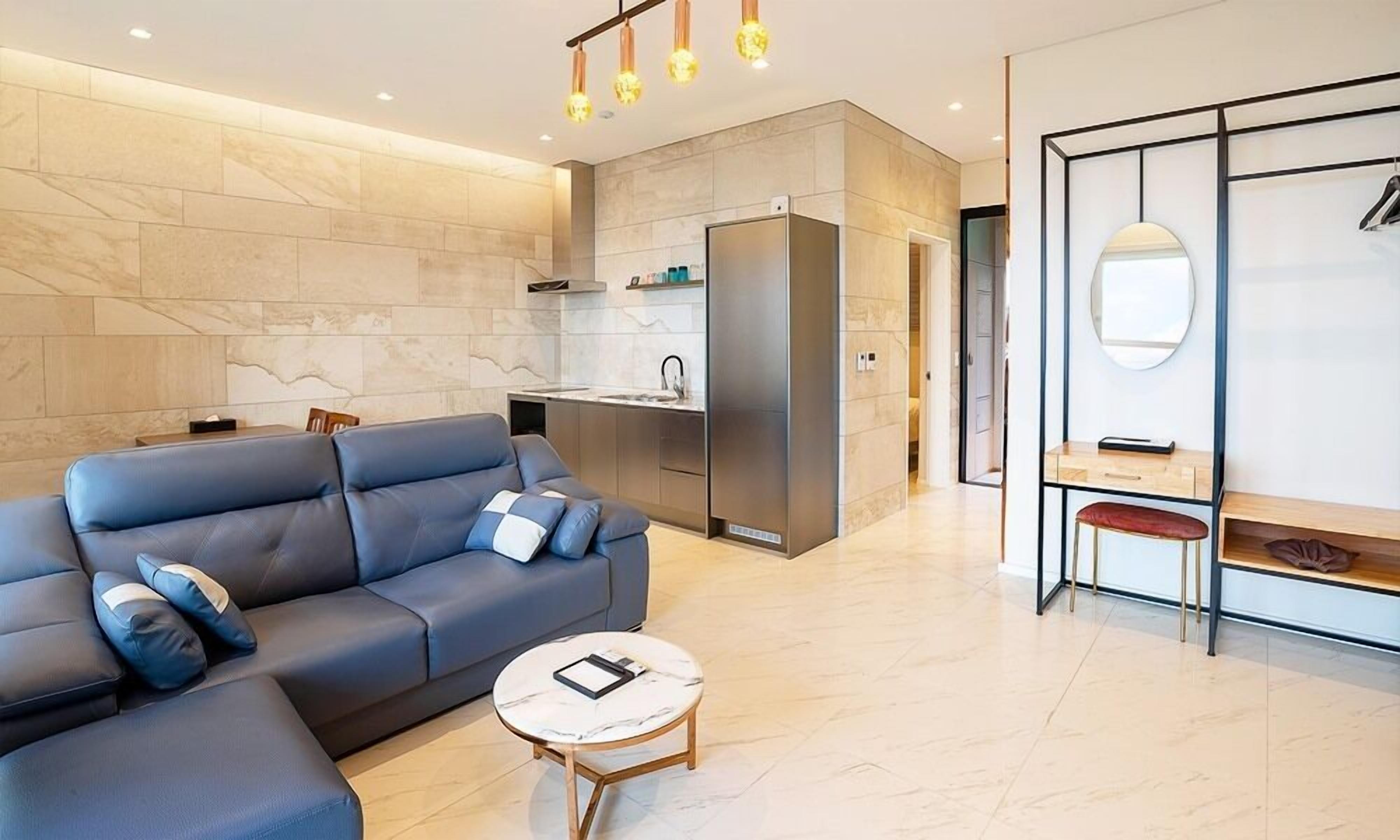 Uma sala de estar moderna com um sofá, uma mesa redonda pequena e uma cozinha com geladeira e armários.