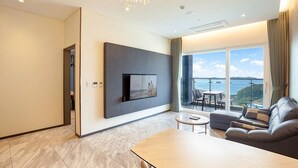 Habitación de hotel moderna con un televisor grande montado en la pared, un sofá, una mesita y un balcón con vista al mar.
