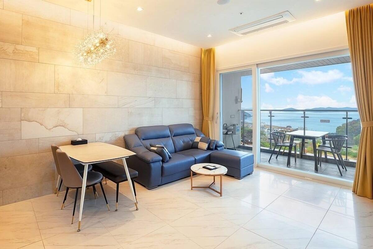 A modern living room with a blue sofa, a small round table, and a dining area with chairs.