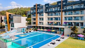 Un hotel moderno con piscina en la azotea, varios balcones y un cartel que dice "ELIJAH RESORT".