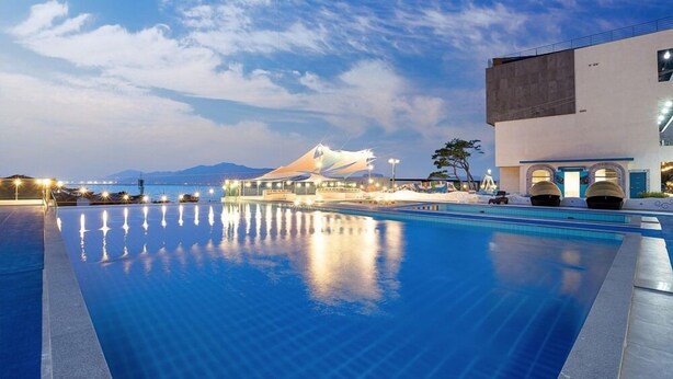 Una piscina con vista a un edificio moderno y montañas al fondo.