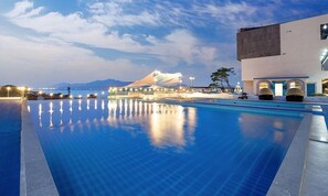 A swimming pool with a view of a modern building and mountains in the background. - Elijah Resort (Incheon)