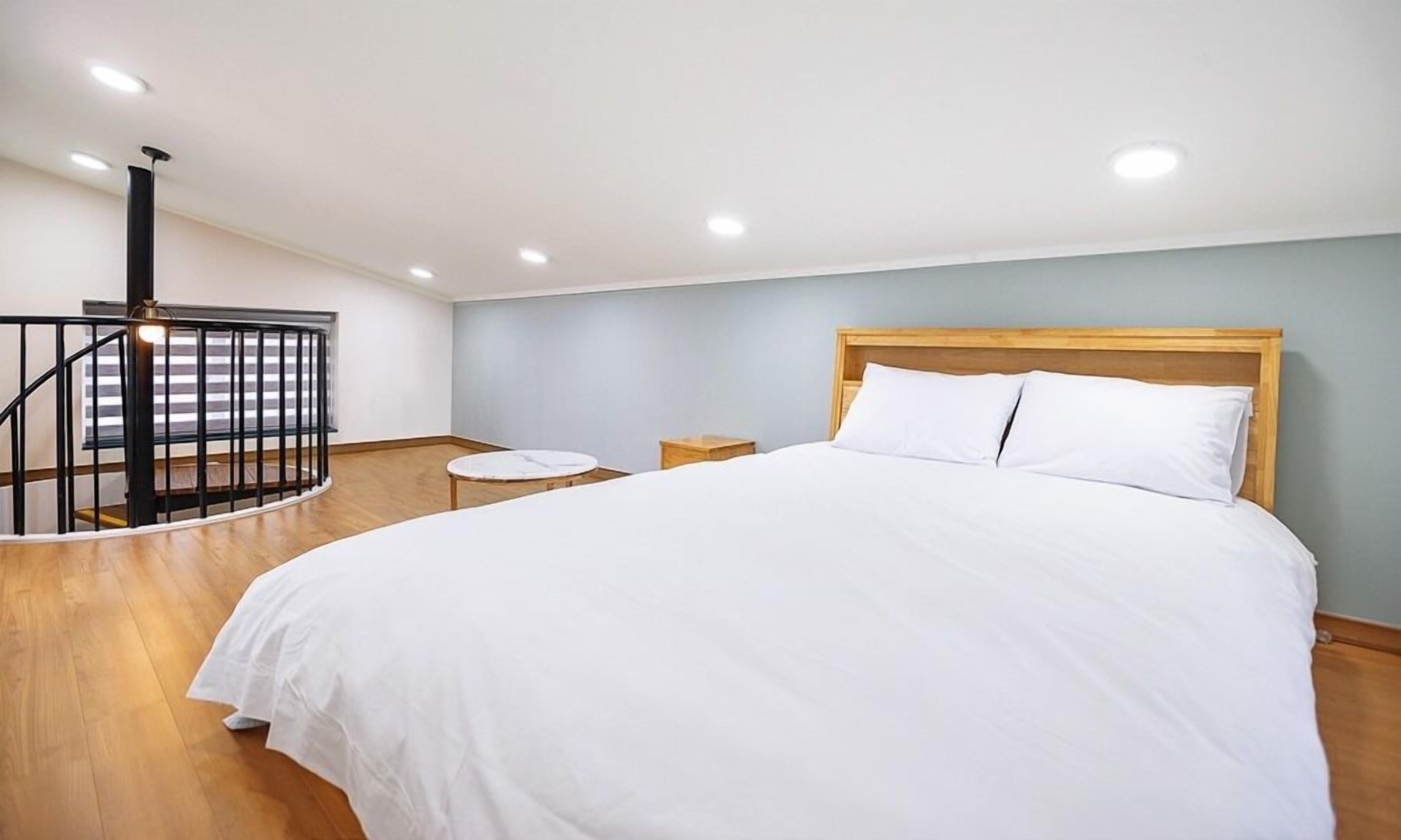 Un dormitorio con una cama grande, cabecera de madera, una mesita redonda pequeña y una escalera en espiral negra.