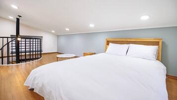 Un dormitorio con una cama grande, cabecera de madera, una mesita redonda pequeña y una escalera en espiral negra.