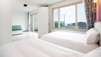 A modern hotel room with two beds, a large window with a city view, and a balcony.