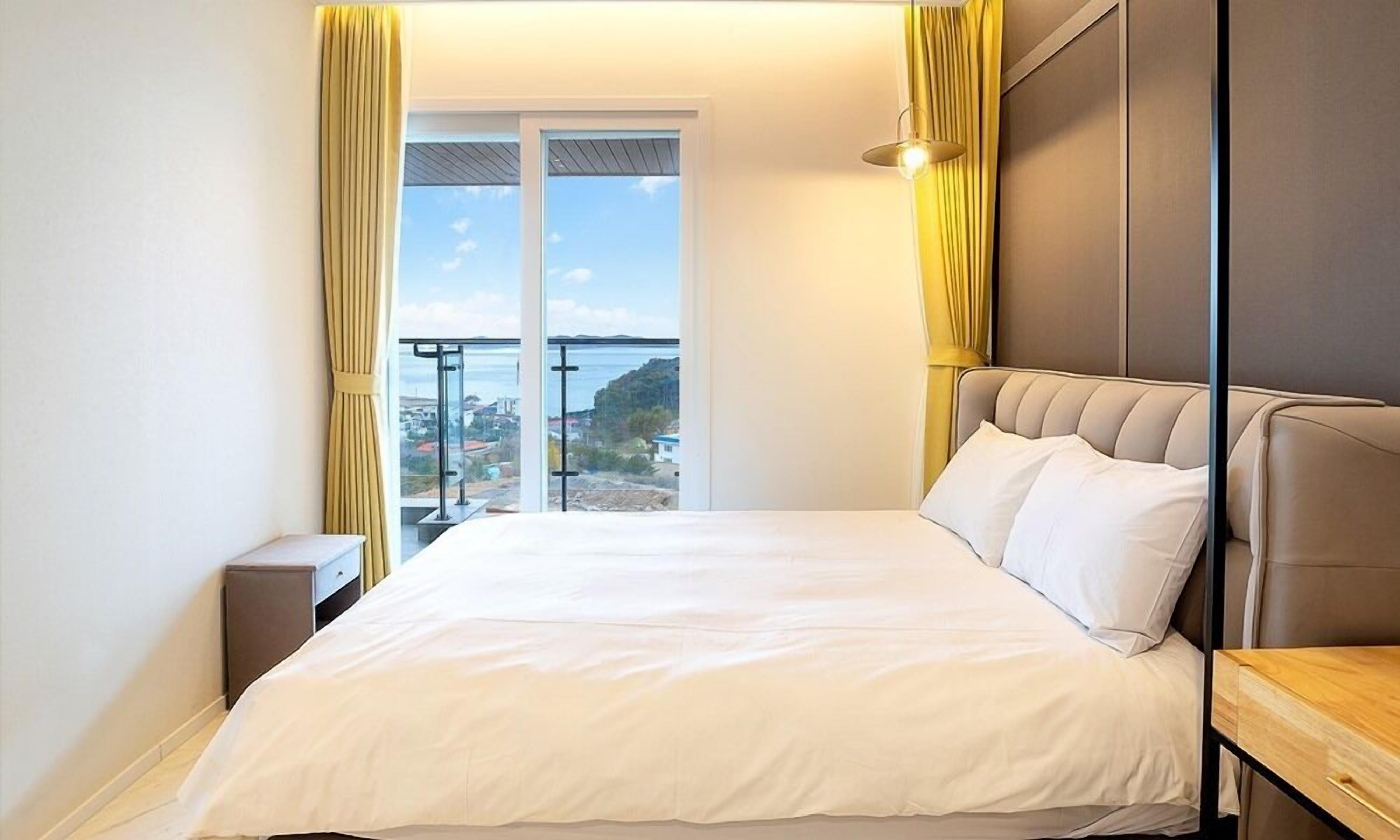 Habitación de hotel con cama, mesita de noche, mesita auxiliar de madera y vista al mar a través de una puerta corrediza.