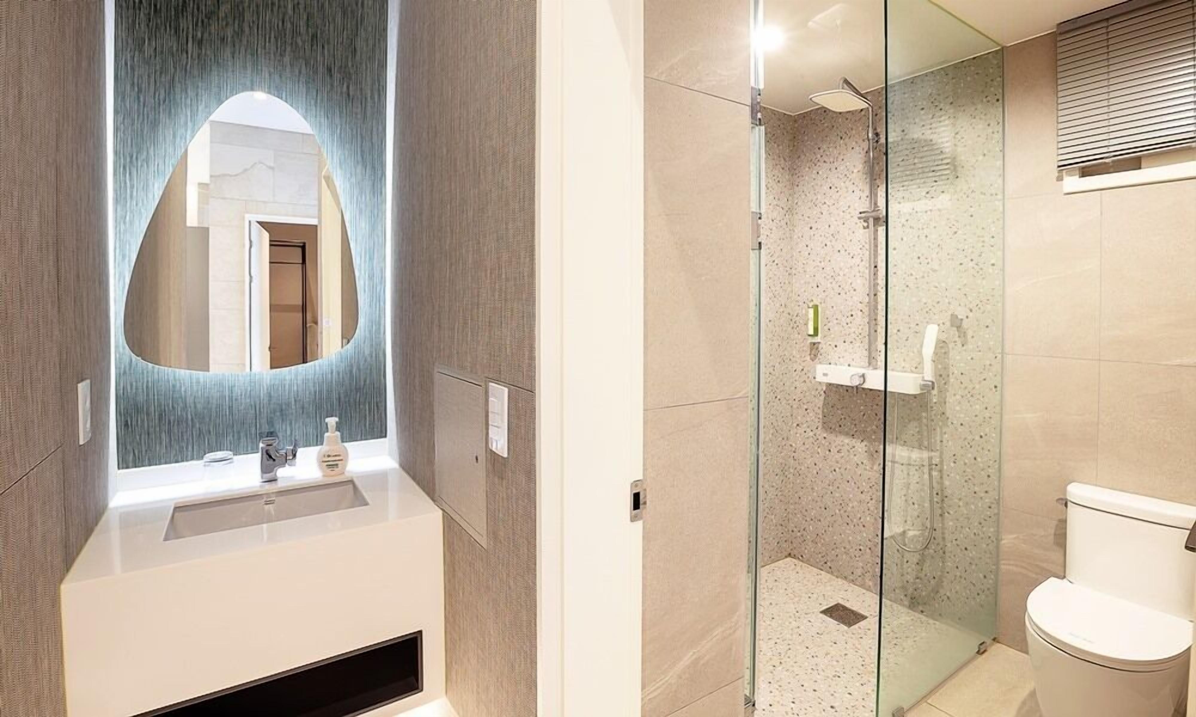 A modern bathroom with a large mirror, a glass shower enclosure, and a toilet.