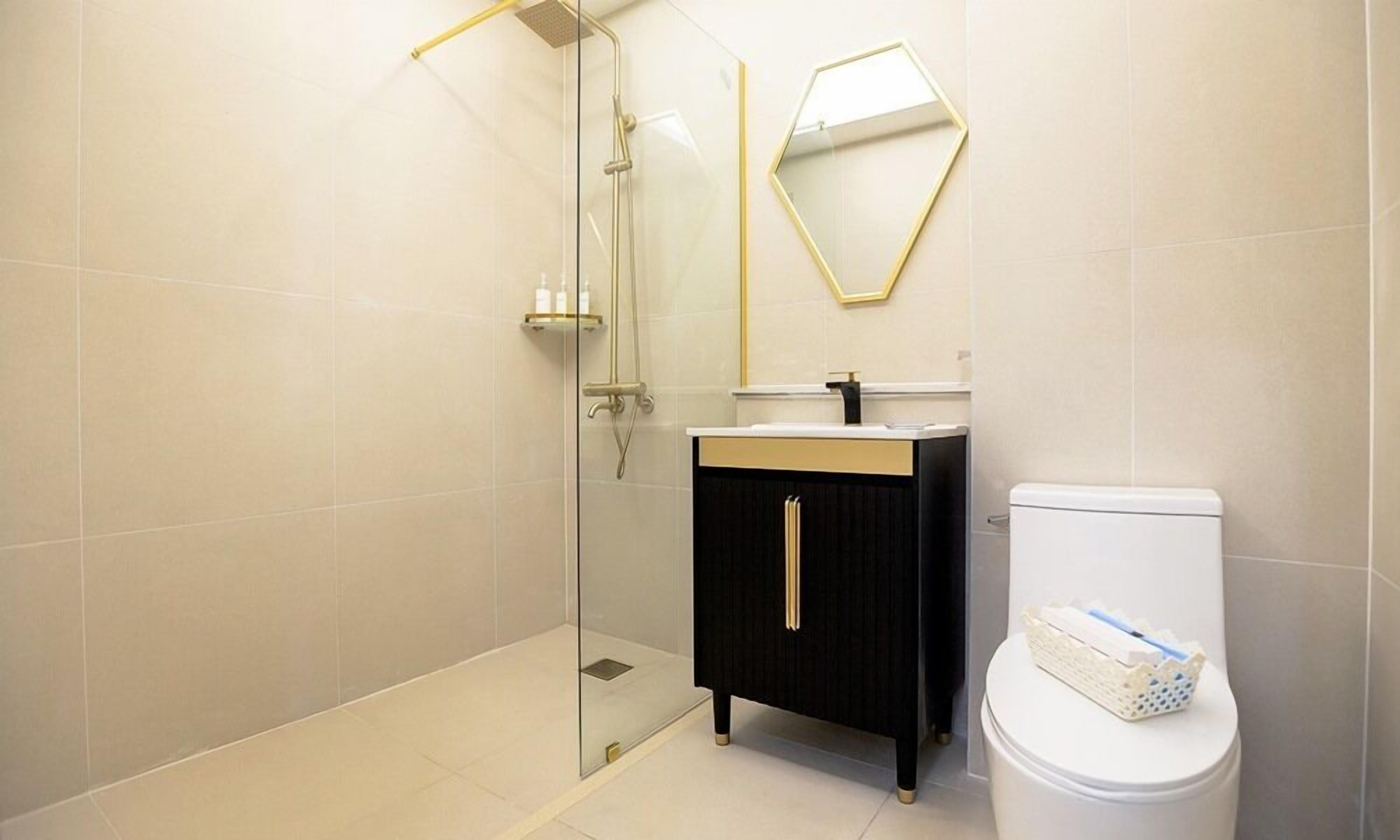 Une salle de bain moderne avec une douche à l’italienne en verre, un meuble-lavabo noir avec des poignées dorées et des toilettes blanches.