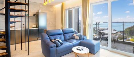 A modern living room with a blue sofa, a round coffee table, and a view of the sea through large windows.