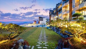 Un hotel moderno con piscina, mobiliario exterior y un jardín bien cuidado.