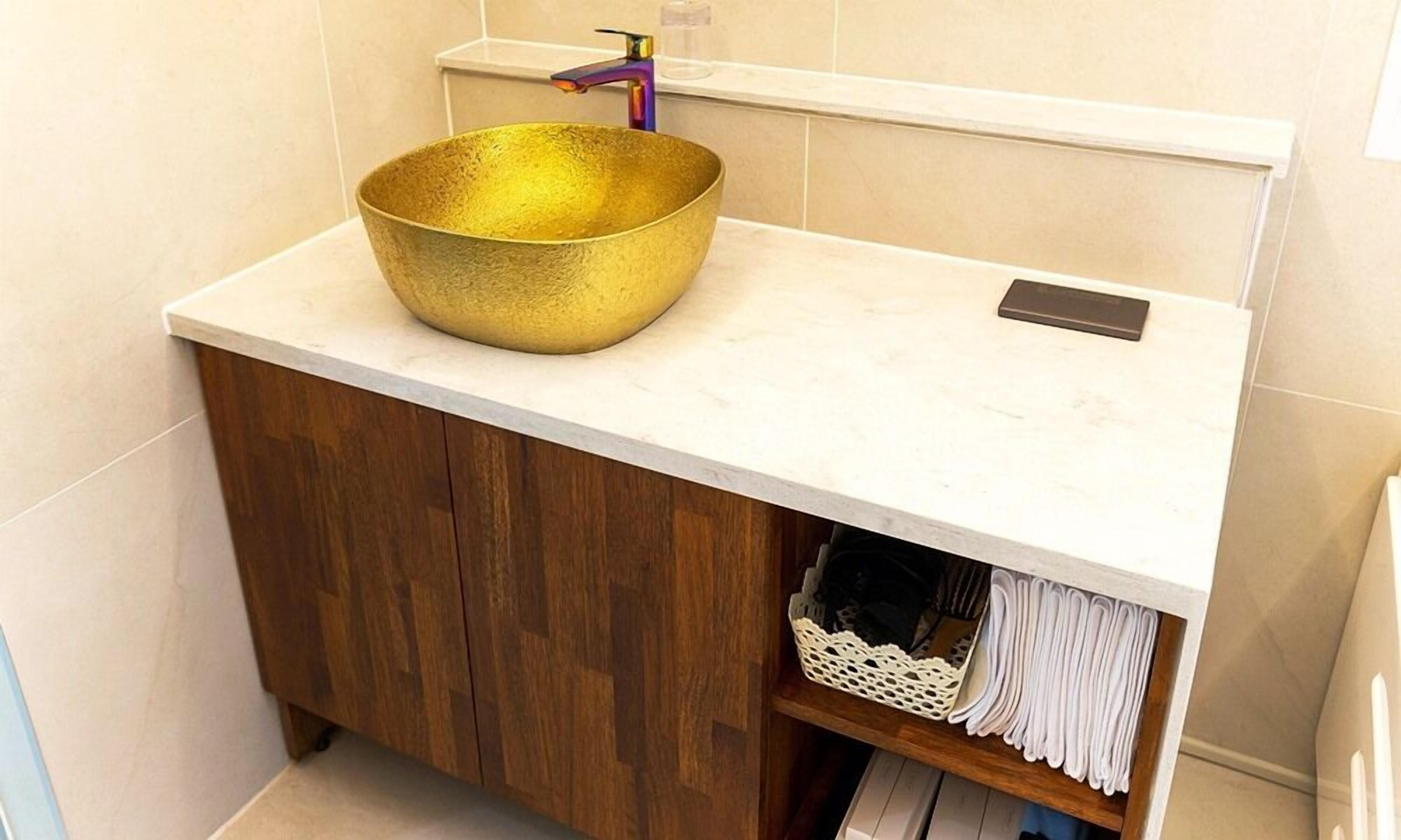 A bathroom with a gold bowl sink, a wooden cabinet, and a towel rack.