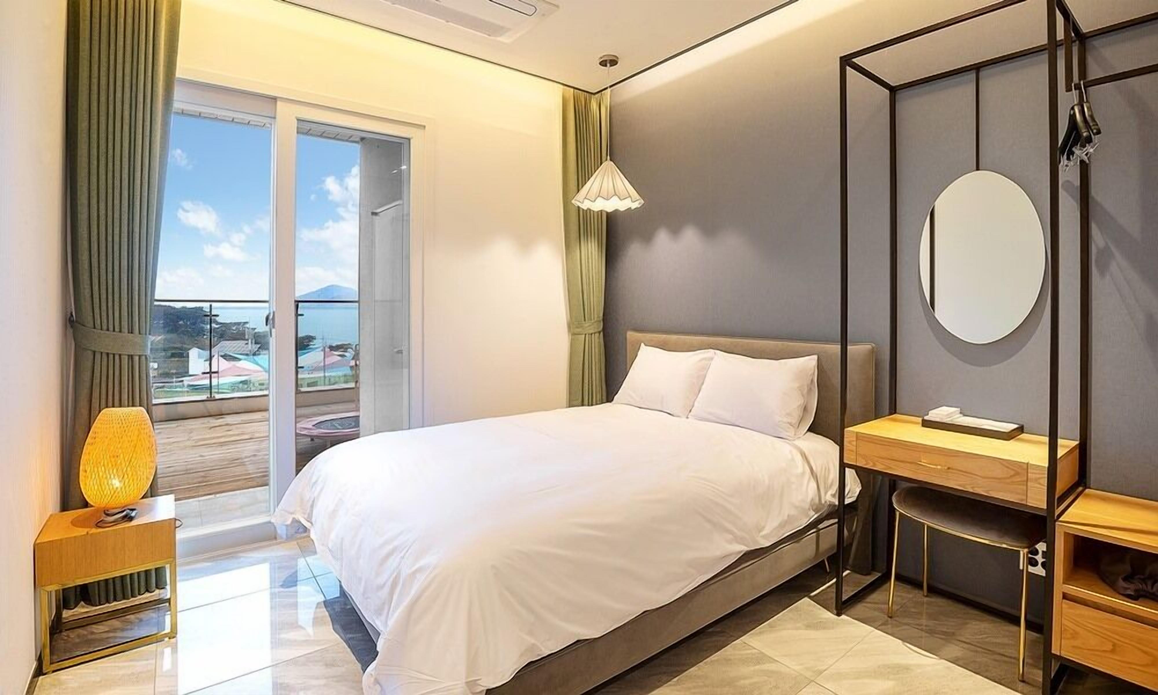 Habitación de hotel moderna con una cama grande, un escritorio y vista al mar a través de una puerta corrediza.