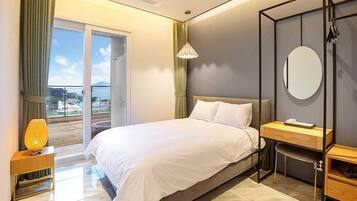 Habitación de hotel moderna con una cama grande, un escritorio y vista al mar a través de una puerta corrediza.