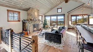 A spacious living area with a stone fireplace, a large sofa, and a view of mountains through large windows.
