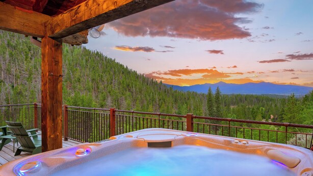 A hot tub on a wooden deck with a view of a forest and mountains.