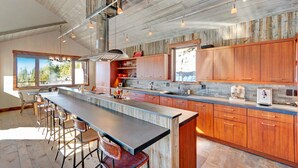 A modern kitchen with a large island, wooden cabinets, and pendant lighting.