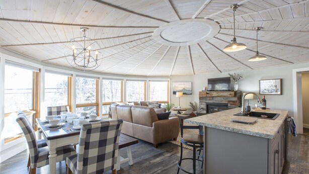 A spacious living area with a high ceiling, a dining table with chairs, a sofa, and a kitchen area with a sink and countertop.