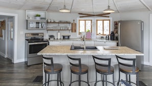 A kitchen with a central island, bar stools, stainless steel appliances, and pendant lighting.