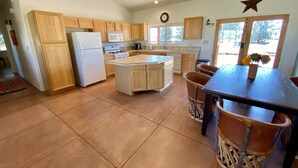 A modern kitchen with wooden cabinets, a central island, and a dining area with chairs. - Sunset Ride Ranch /Foreman's house (Elgin)