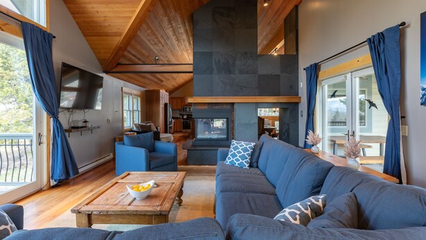 A modern living room with a fireplace, blue sofas, wooden flooring, and a large window with curtains. - JHRL - Lookout Lodge, short walk to base of Jackson Hole Mountain Resort (Teton Village)