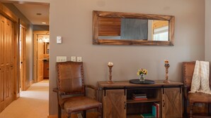 A hallway with wooden doors, a wooden chair, a wooden cabinet with books, and a mirror on the wall. - JHRL - Lookout Lodge, short walk to base of Jackson Hole Mountain Resort (Teton Village)